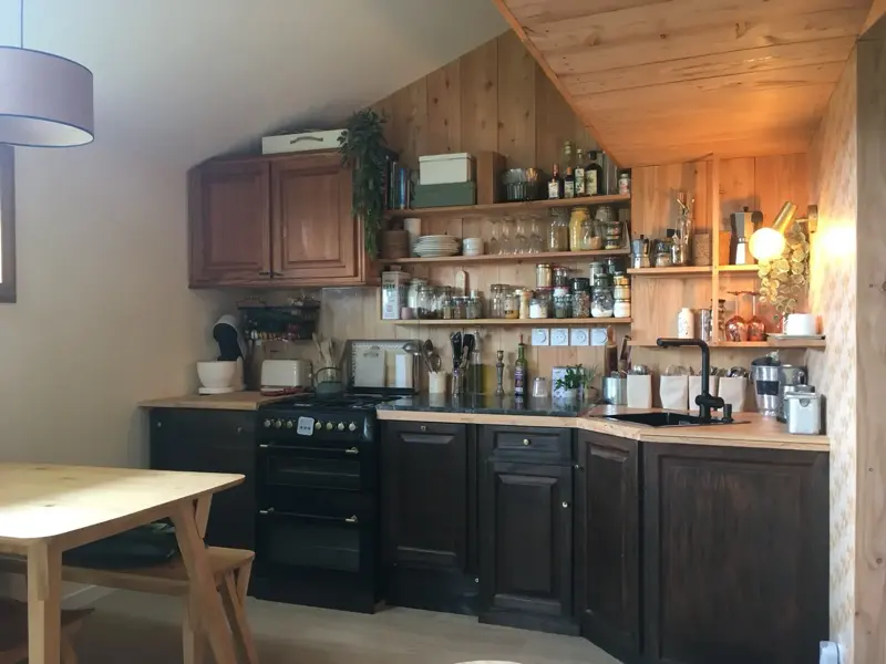 Cuisine réalisée dans une grange rénovée : façades noires, plan de travail bois et mur en lambris ancien